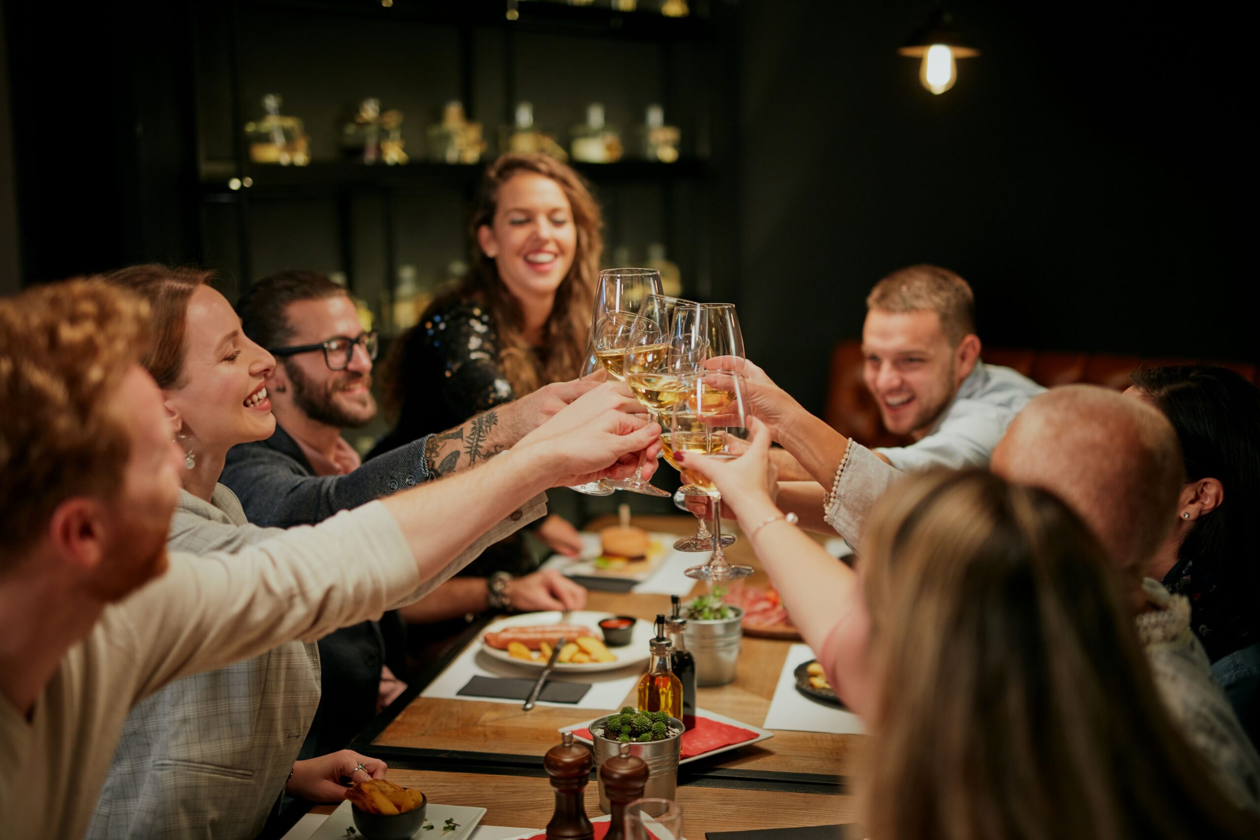 Mehrere Personen sitzen zusammen an einem Tisch und stoßen an 